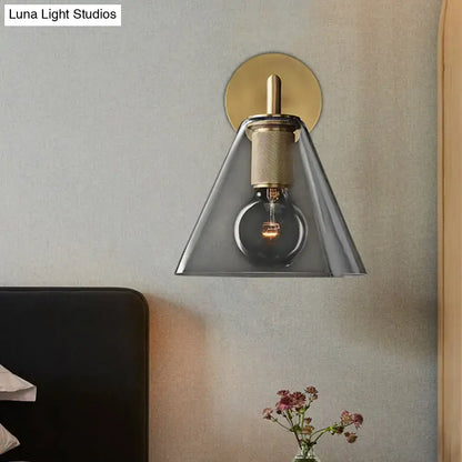 Modern wall light with brass finish, textured stem, gray glass cone shade, direct wired electric for bedroom use