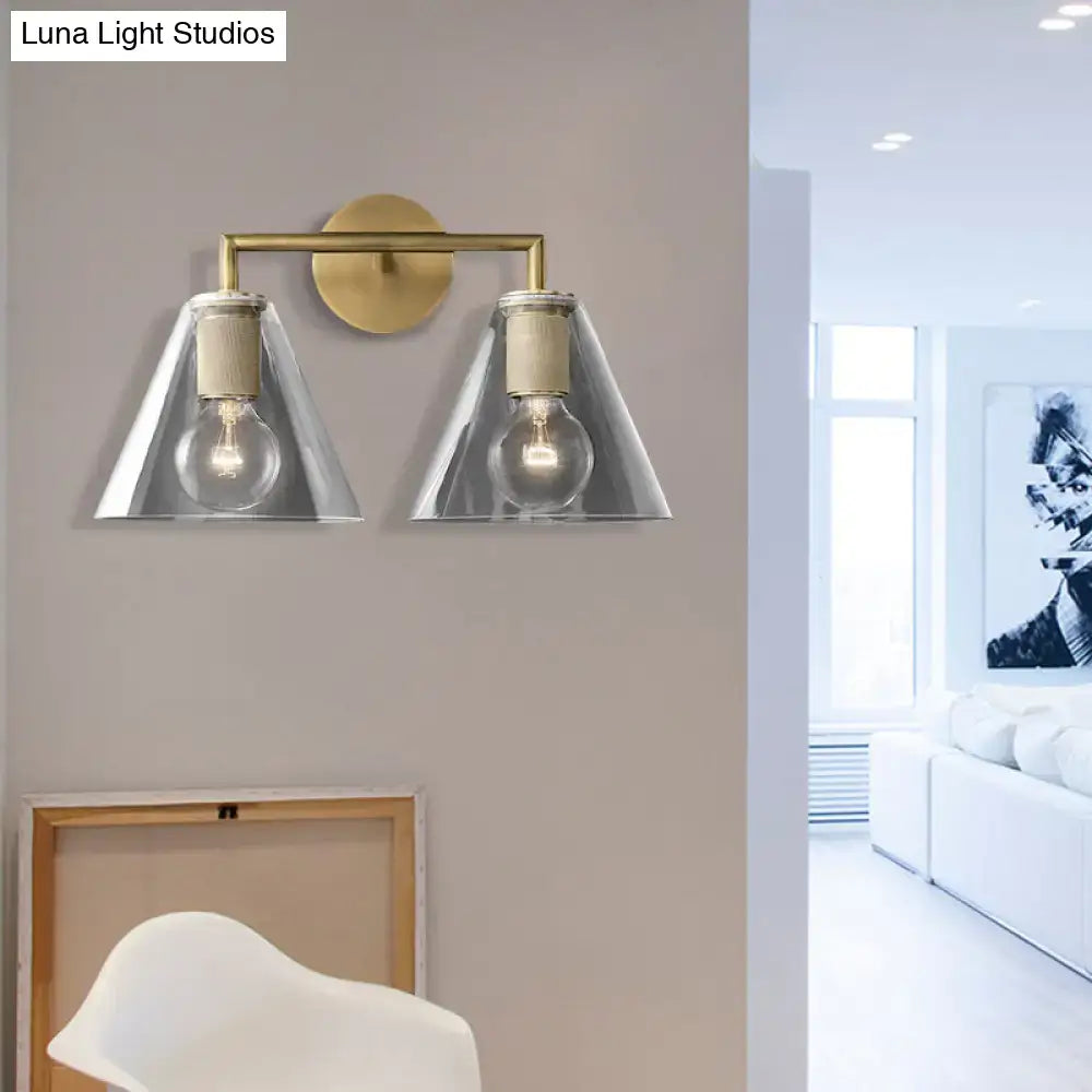Brass-finished modern wall light with two clear glass cone shades and exposed bulbs direct wired electric design