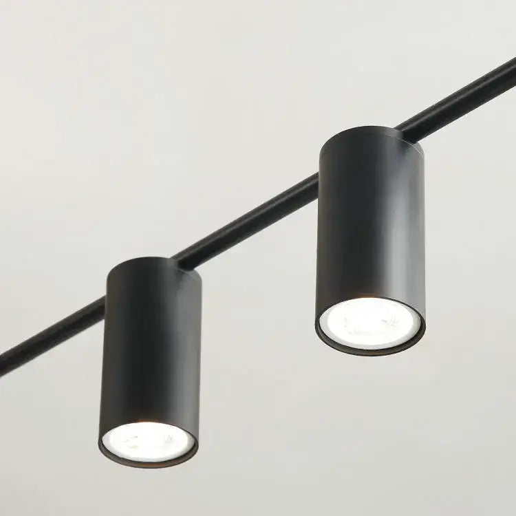 Modern black and brass minimalist dining room linear pendant light with black cylindrical track lights and recessed led bulbs