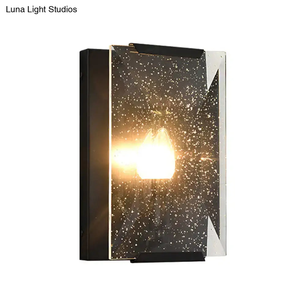 Modern black and brass sconce light with speckled glass panel and black brass finish for bedroom wall illumination