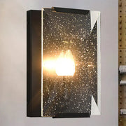 Modern black brass finish sconce light with speckled glass panel diffusing warm light for bedroom wall lamp