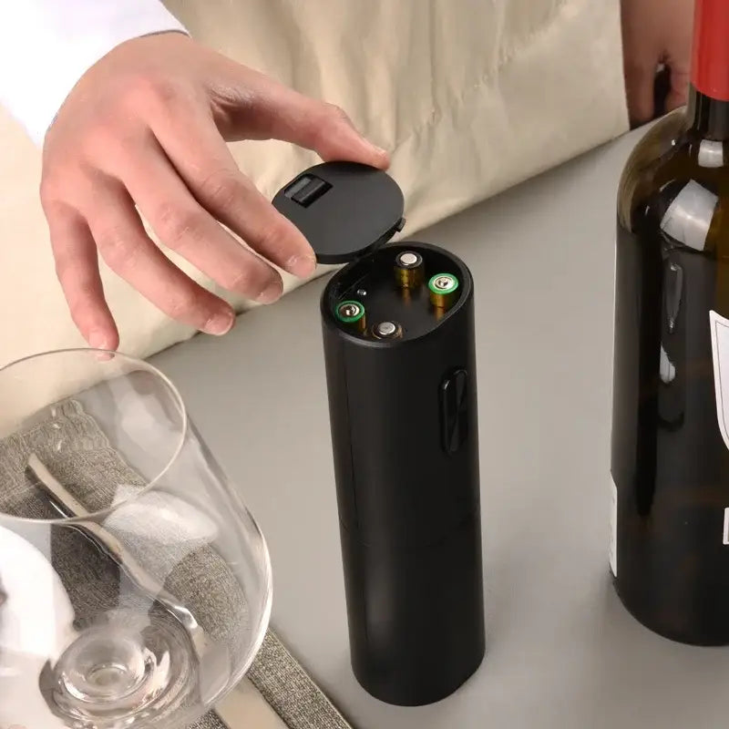 Modern black brushed metal electric wine opener with hinged lid and visible battery compartments for easy use