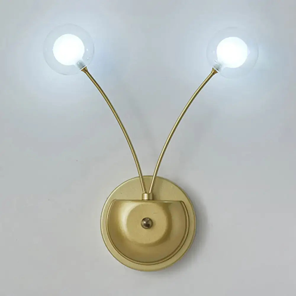 Modern gold-toned cast iron wall sconce with two curved arms and clear glass globes measuring inches fixture
