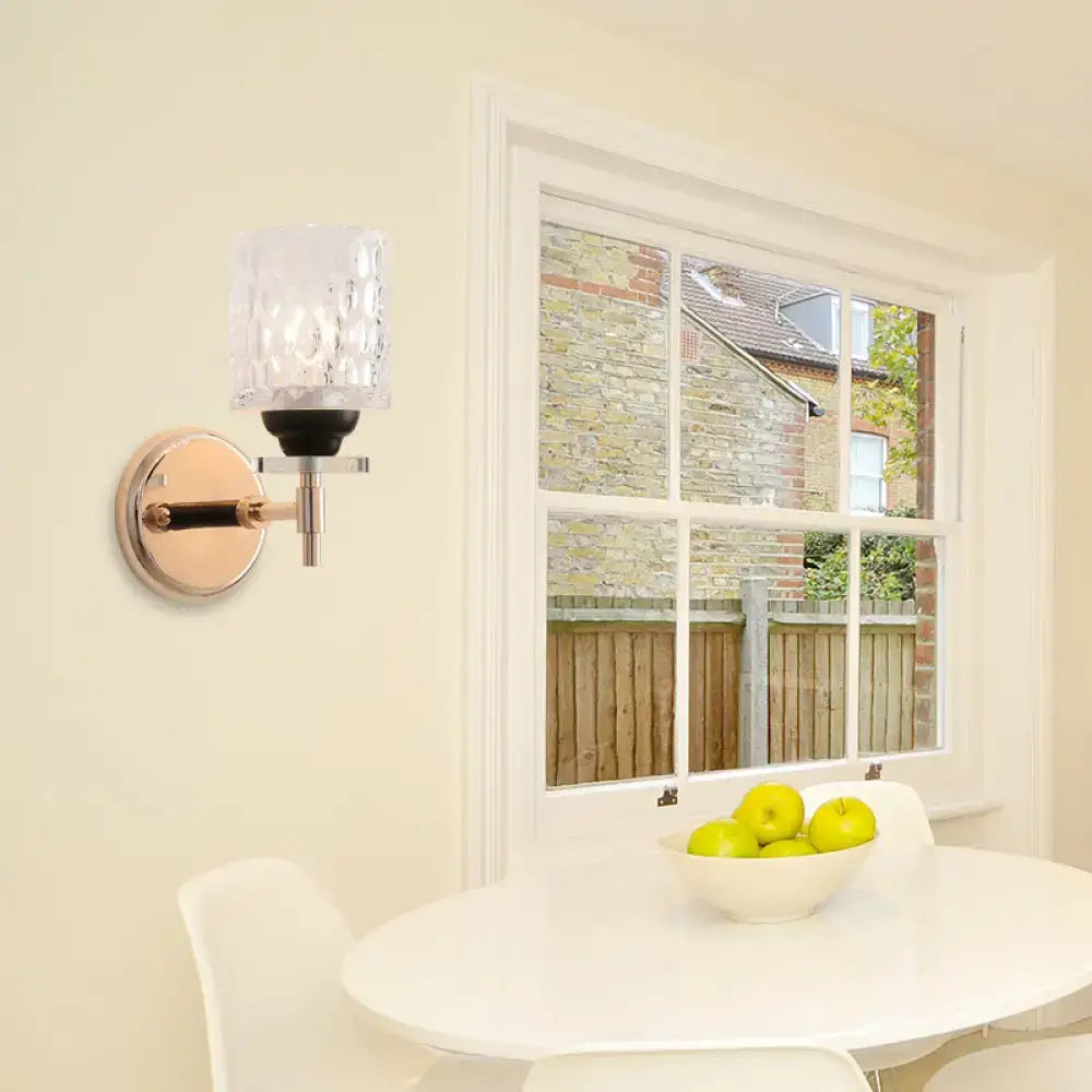 Modern black chrome wall sconce featuring a dimpled glass cylinder with rose gold metal accents for bedroom lighting