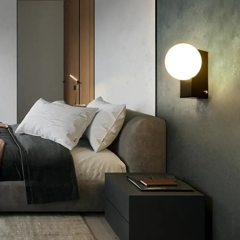 A sleek modern black & chrome decorbites glass ball wall sconce with a glowing white globe for bedroom lighting