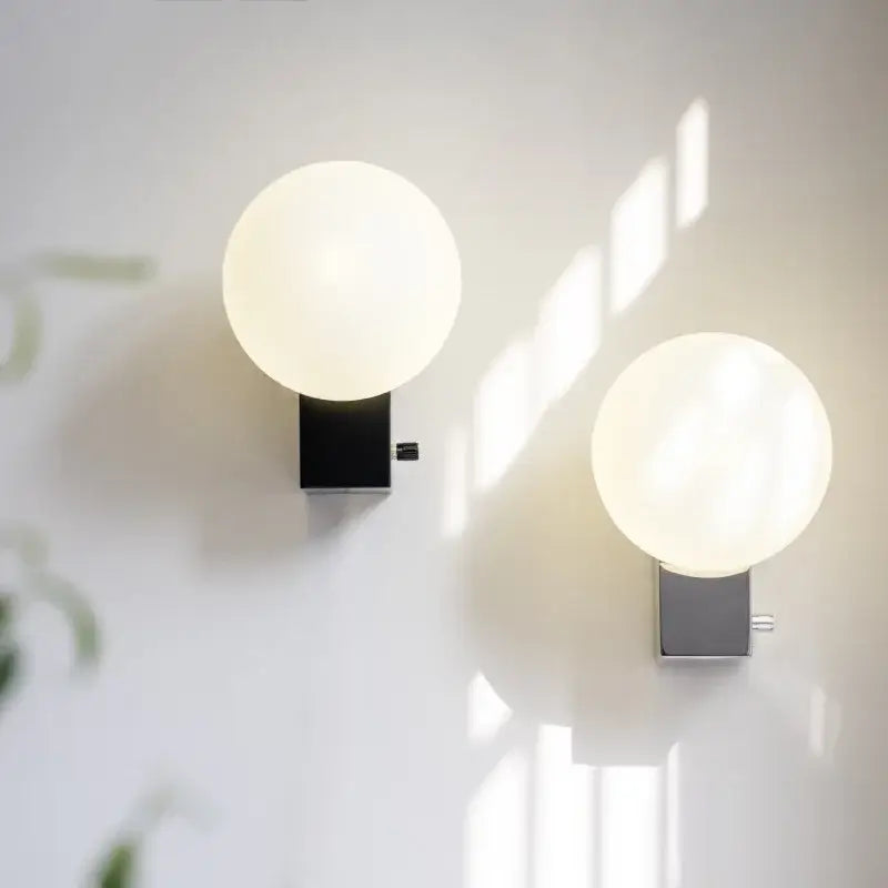 Two minimalist decorbites glass ball wall sconces with black and chrome bases for modern bedroom lighting