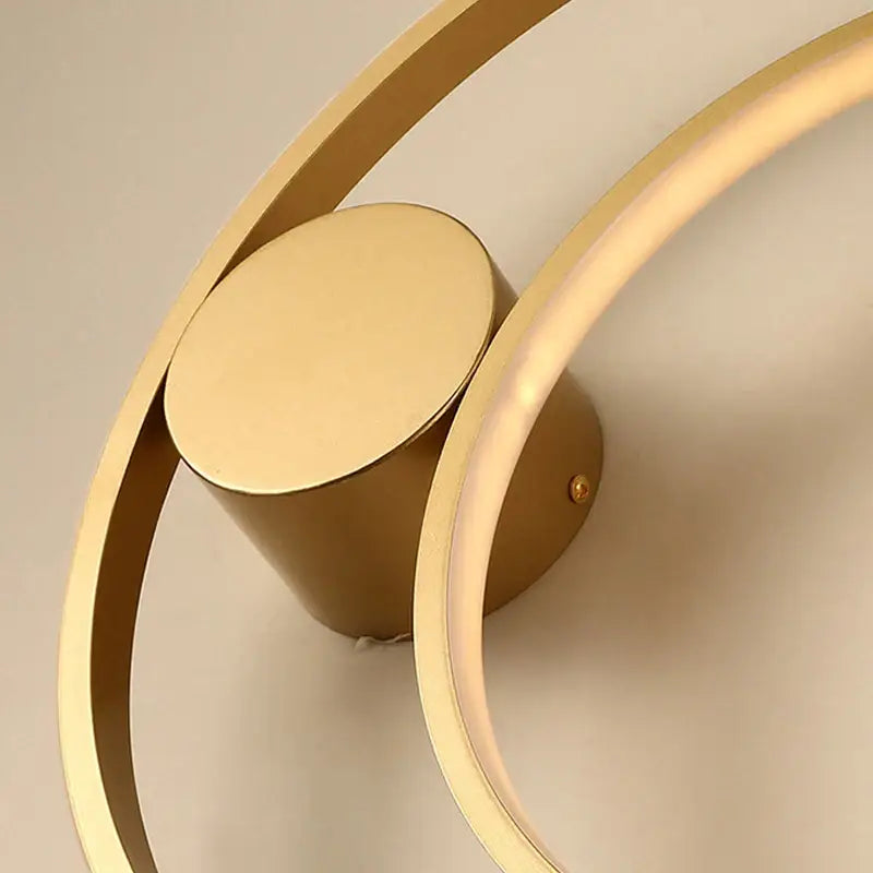 Gold-toned modern led wall lamp with sleek circular rings and cylindrical base for minimalist bedroom sconce lighting