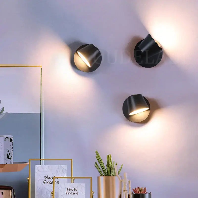 Three modern black conical led wall lamps with sleek angular designs emitting warm light for bedroom reading