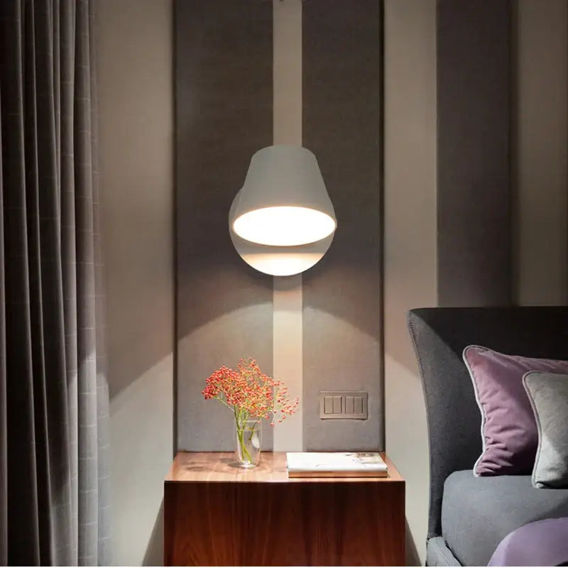 Modern black conical led wall lamp paired with a sleek white pendant lamp above a wooden nightstand in bedroom reading light setting