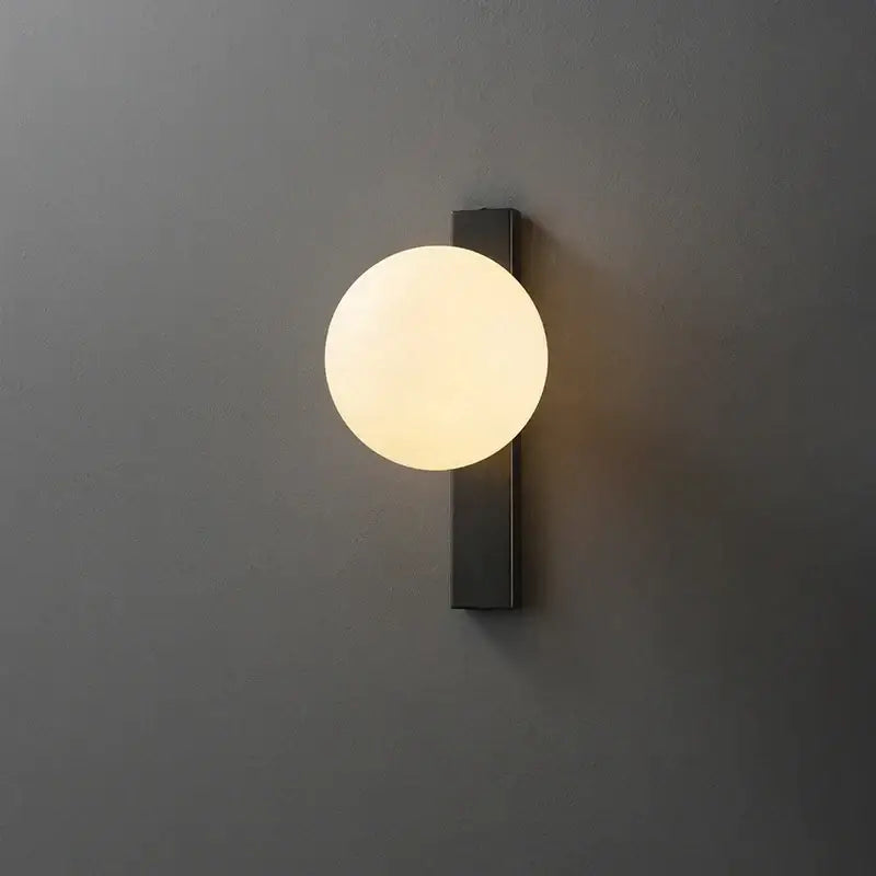 Modern black copper globe led wall sconce featuring a glowing frosted glass globe for bedroom lighting