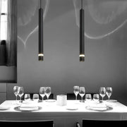 Two sleek black decorbites cylinder pipe pendant lights hang above a dining table for modern dining room decor