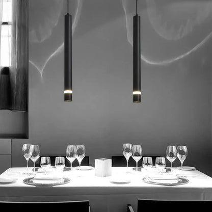 Two sleek black decorbites cylinder pipe pendant lights hang above a dining table for modern dining room decor