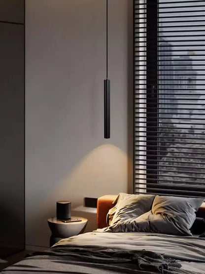 Modern black cylindrical cord pendant light with sleek minimalist design and black finish hanging above bedroom bed