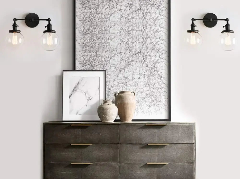 Modern black double ball heads globe glass wall sconce above dark gray textured dresser with gold-toned handles