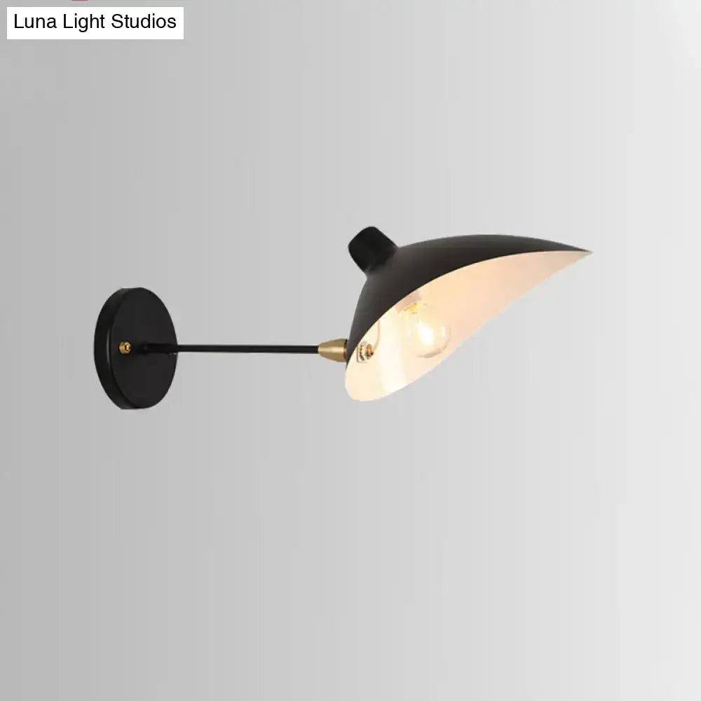 Modern black wall lamp with duckbill shade, brass accents, and curved arm designed as a bedroom sconce