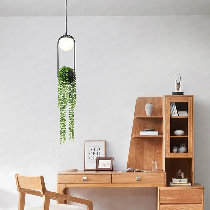 Modern black flower pot pendant lights featuring a black-framed globe bulb and hanging green trailing plant decorbites black flower