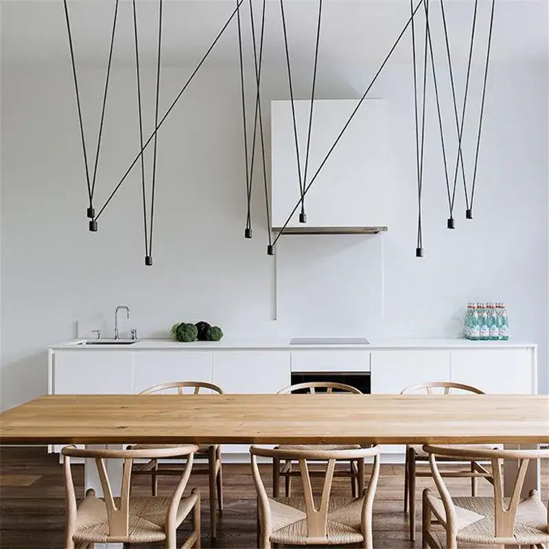 Modern black geometric led wire pendant light with wire frame design hanging above a minimalist kitchen and dining table