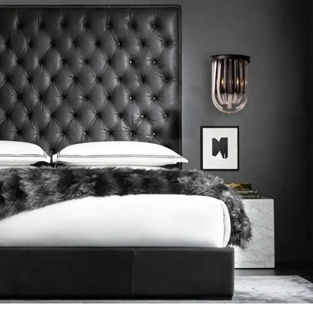 Modern black glass and metal semi oval wall light with black finish mounted above a black tufted leather headboard with diamond pattern stitching