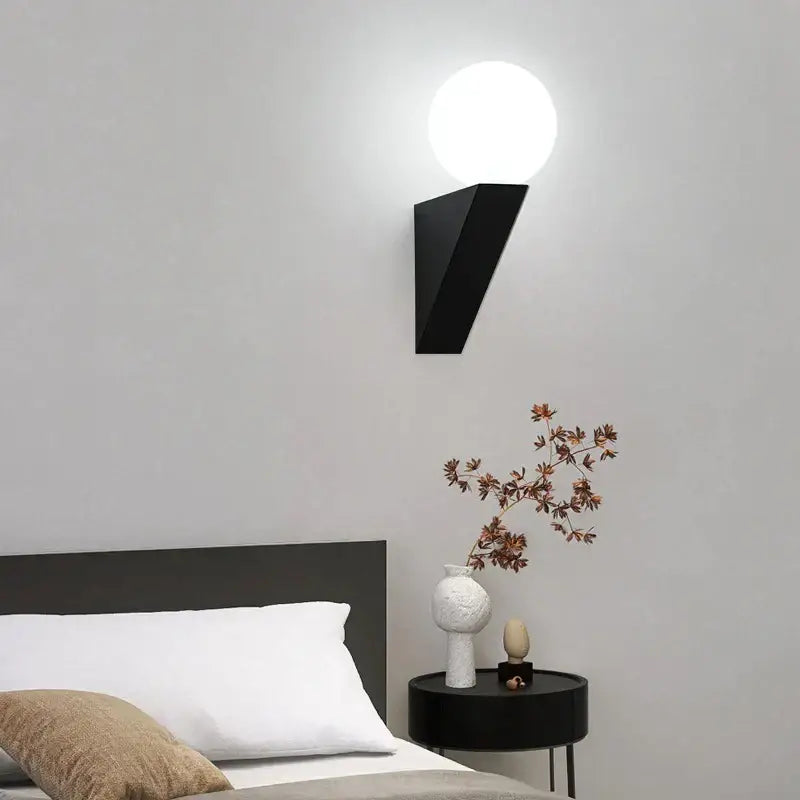 Modern black glass ball wall lamp featuring a black geometric wall sconce with a round white globe light for bedroom use