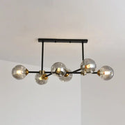 Modern black island pendant light with six clear glass globe bulbs and brass accents for dining room lighting