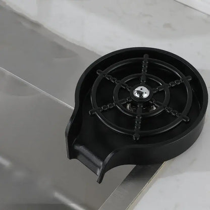 Modern black glass rinser sink with a black plastic coffee cup holder featuring a ship’s wheel design and metallic center
