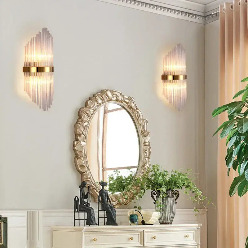 Gold-framed oval mirror with ornate detailing paired with modern black glass rod crystal wall lamp for bedroom use