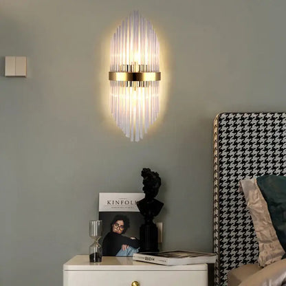 Gold-toned wall lamp with vertical glass rod crystal design radiating from central base for modern bedroom lighting