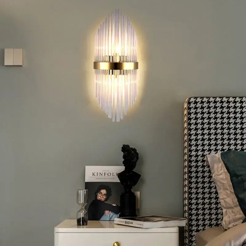 Gold-toned wall lamp with vertical glass rod crystal design radiating from central base for modern bedroom lighting