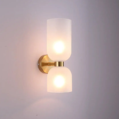 Gold-toned wall lamp with two frosted glass shades emitting warm glow in modern black glass shade wall design
