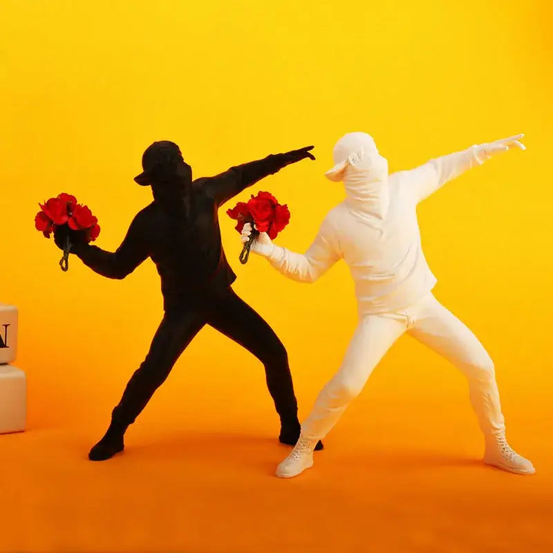Modern black glossy bansky flower thrower sculpture featuring black and white figurines in dance pose holding red flowers