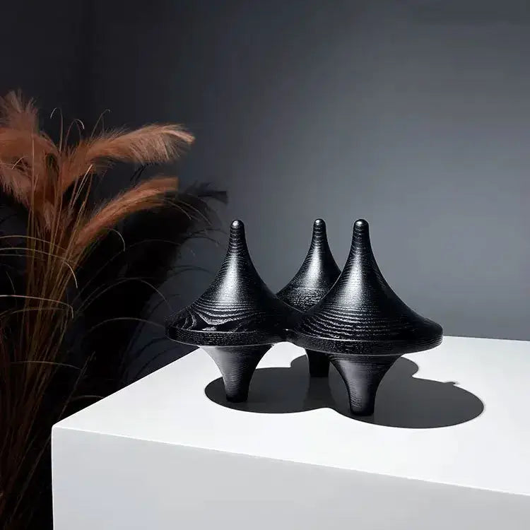 Three sleek black glossy decorbites geometric gyroscope cone sculptures with ribbed surfaces on white living room pedestal