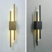 Modern black and gold acrylic pipe wall lamp with brushed brass base and frosted glass diffusers emitting warm light