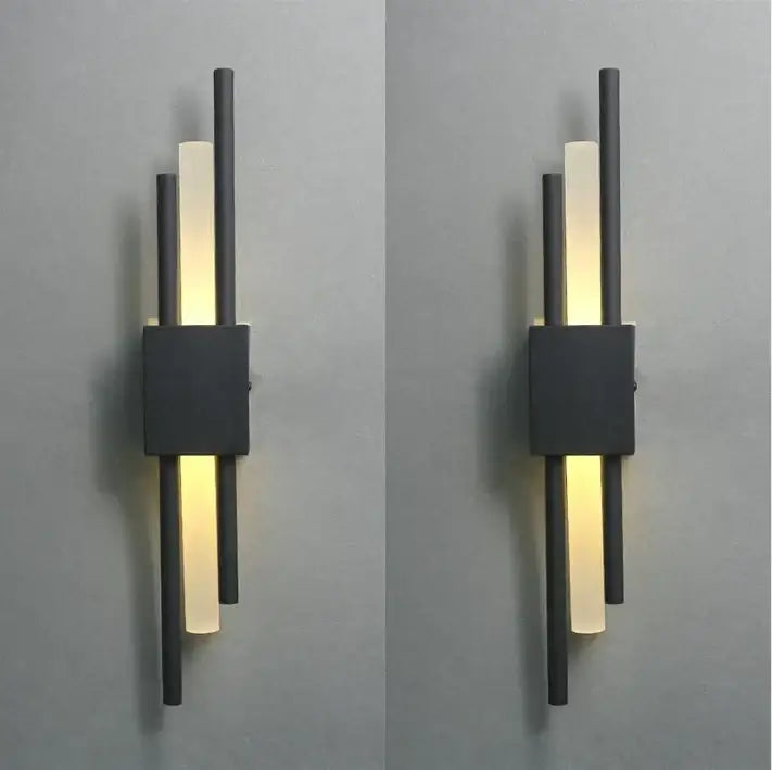 Modern black and gold acrylic pipe wall lamp with three vertical rods and frosted glass panels emitting warm glow