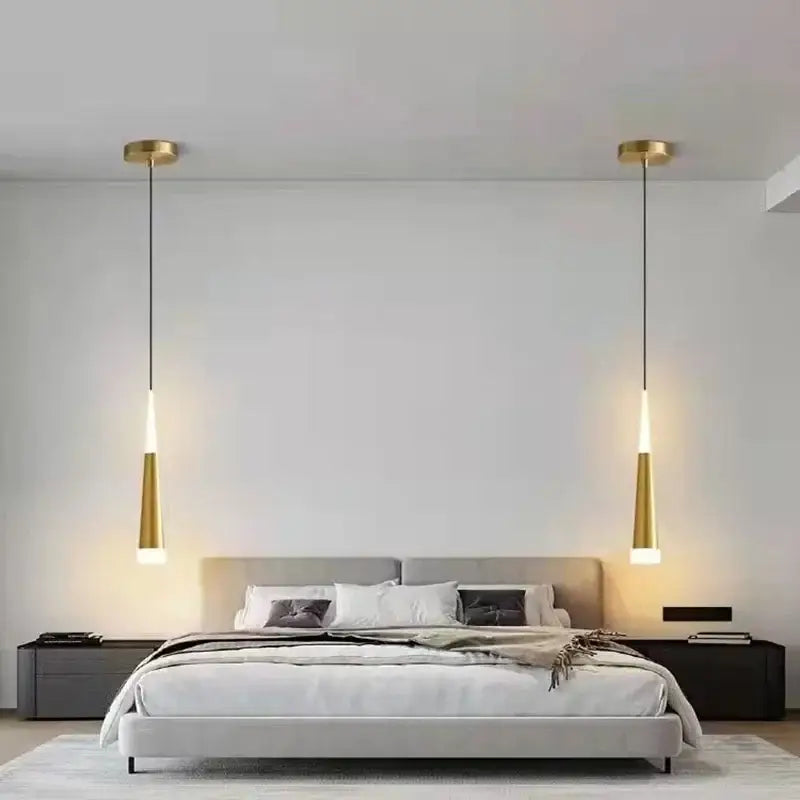 Two sleek gold finished aluminum cord pendant lights with black cords hang symmetrically above a modern bedroom bed