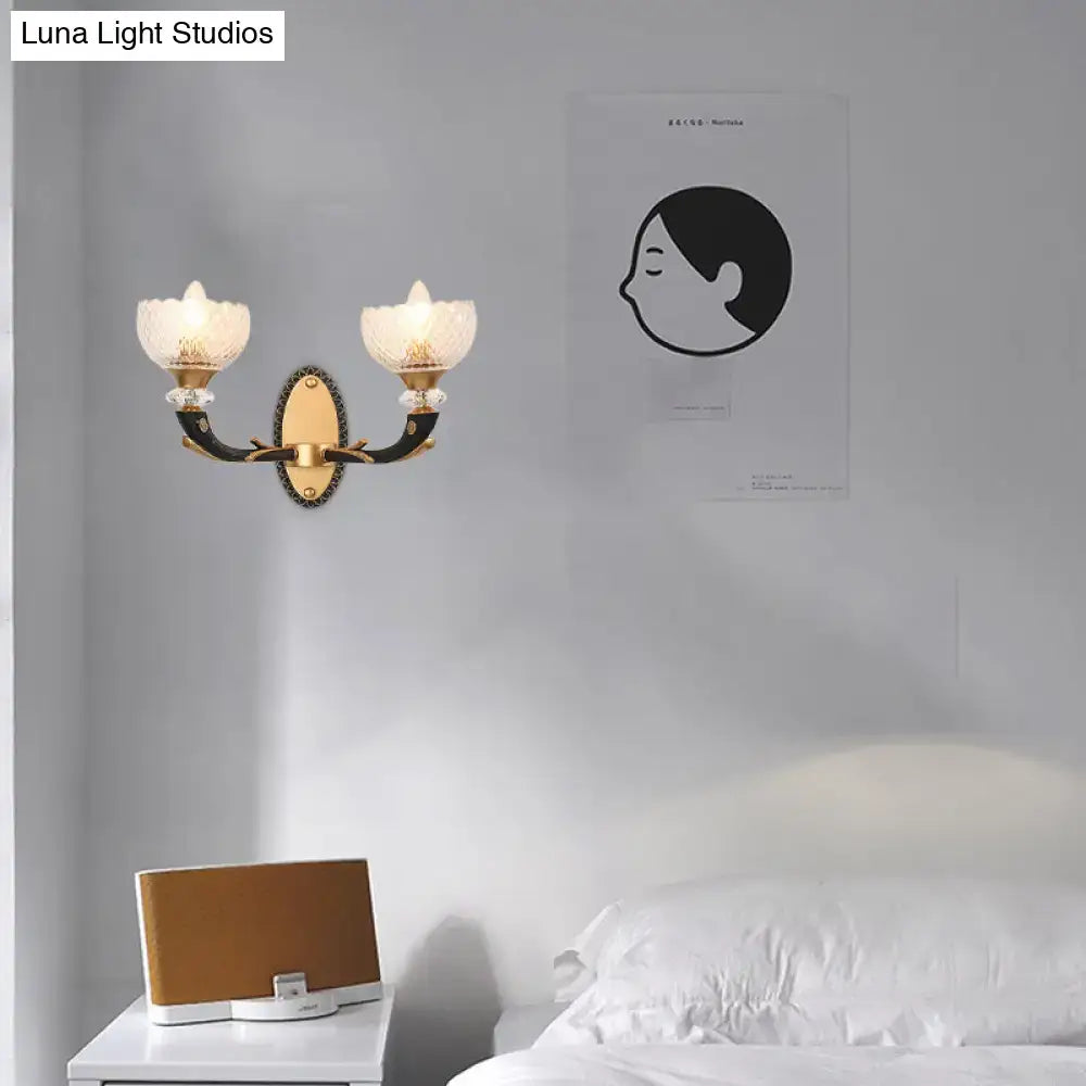 Modern metal black sconce with gold-toned arms and frosted clear prismatic glass flower-shaped shade for bedroom use