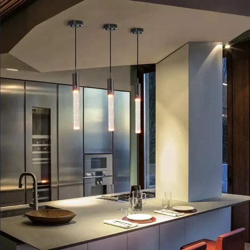 Three modern black and gold decorbites crystal led pendant lamps with cylindrical glass shades hang above kitchen island