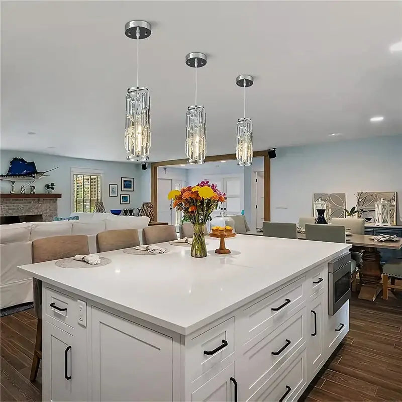 Three modern black and gold decorbites crystal mini pendant chandelier lights with chrome fixtures above white kitchen island