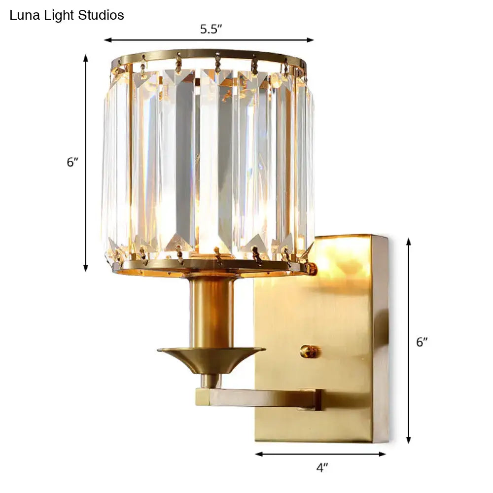 Modern black and gold sconce light fixture with cylindrical crystal shade and brushed brass wired electric power mounting bracket