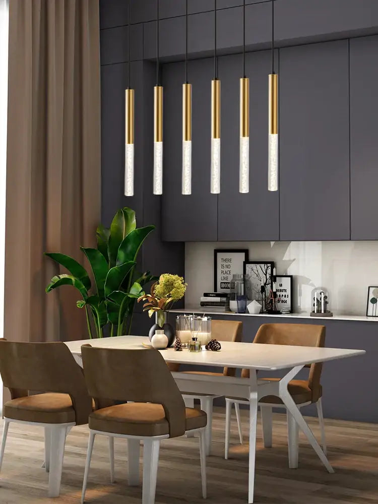 Modern black cylinder pendant lights with gold and frosted glass shades hanging above a kitchen island dining table