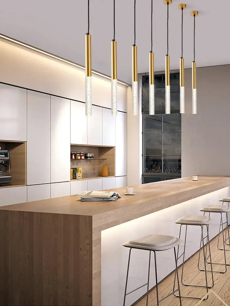 Modern black cylinder pendant lights with gold accents and frosted glass shades hang above a wooden kitchen island
