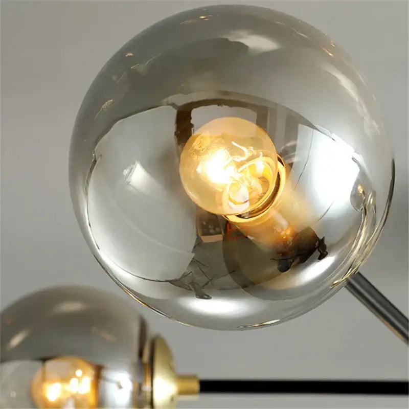 A warm glowing filament bulb inside a reflective chrome shade of a modern black and gold decorbites glass ball led chandelier