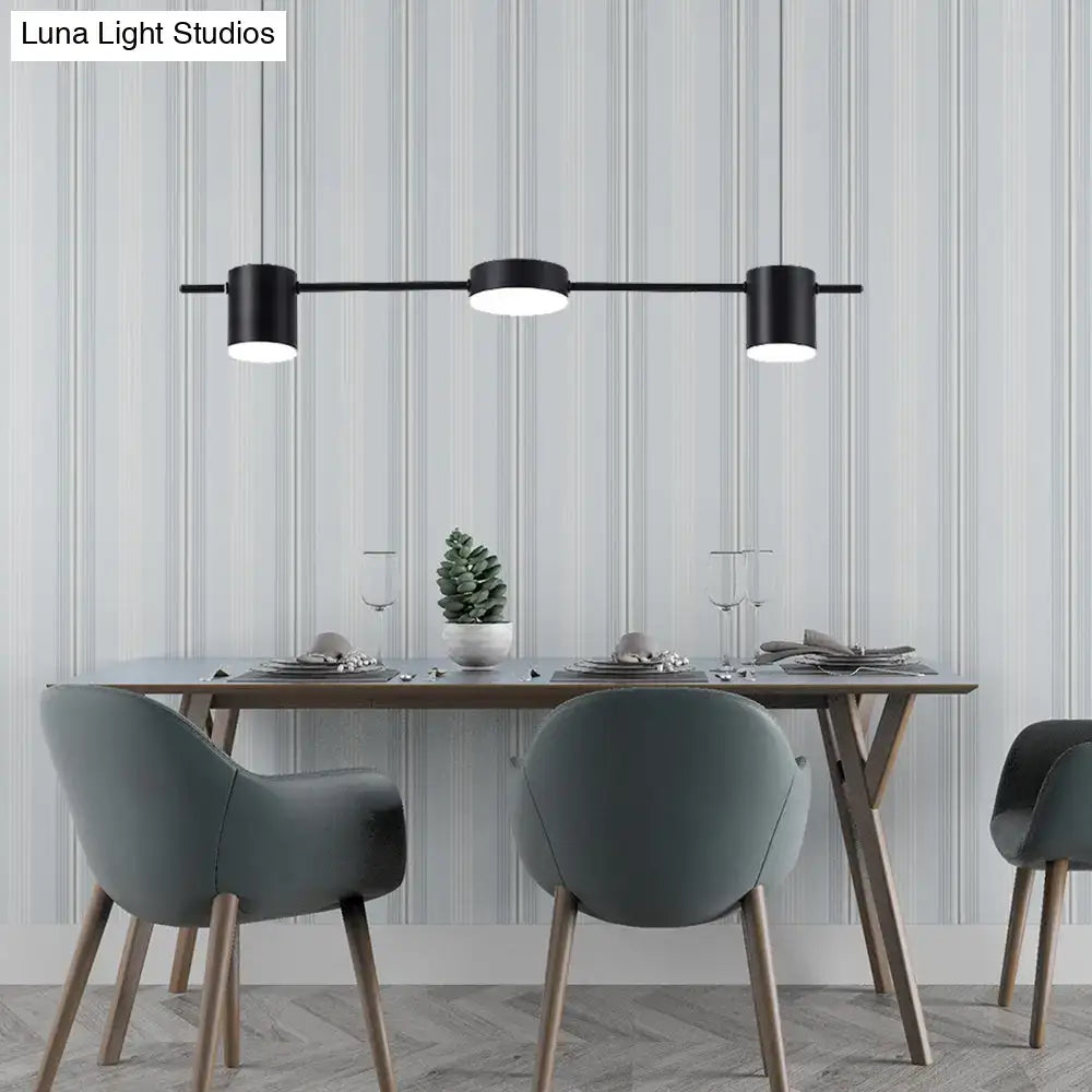 Modern black gold ceiling light fixture with three illuminated cylindrical pendant bulbs above dining table