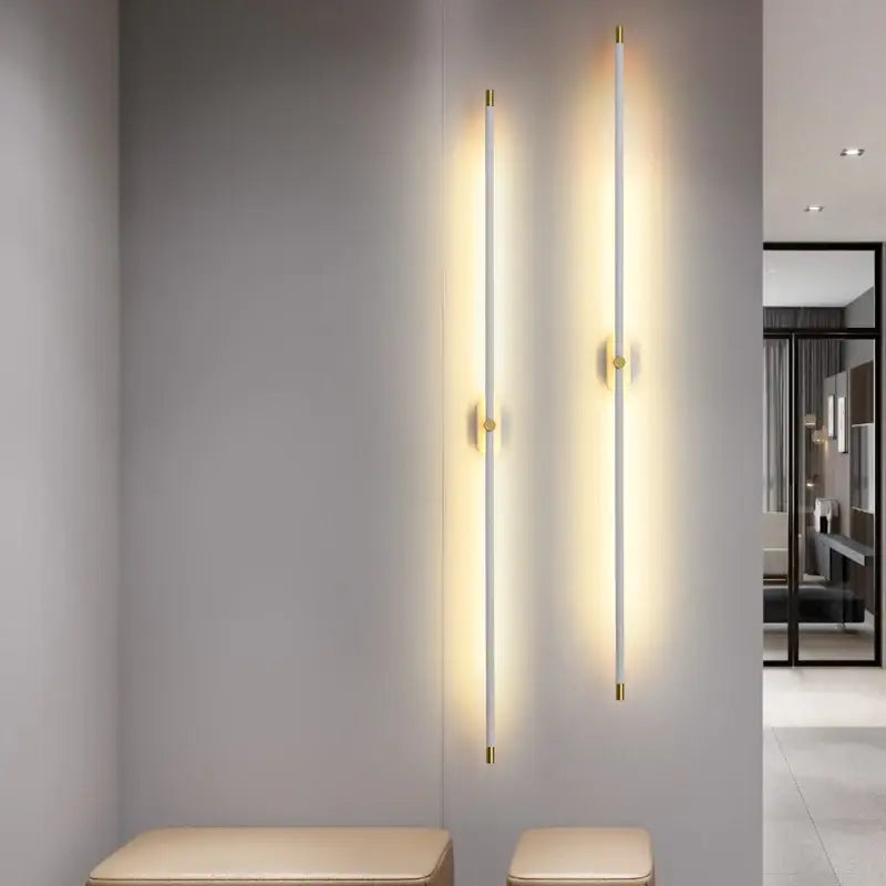 Two slender modern black and gold led strip wall lamps with white cylindrical bodies emit warm light for bedroom decorbites wall lamp