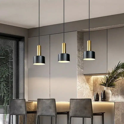 Three modern pendant lights with black cylindrical shades and gold metal finish for kitchen with brushed nickel accents