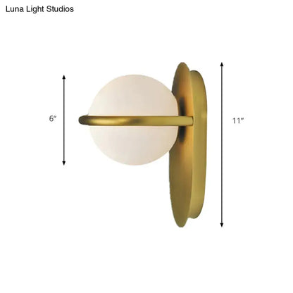 A modern black and gold wall light with milk glass globe and sleek metal backplate for bedroom lighting