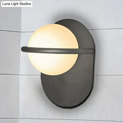 Modern black and gold wall light with matte metal backplate and warm glowing milk glass shade for bedroom use