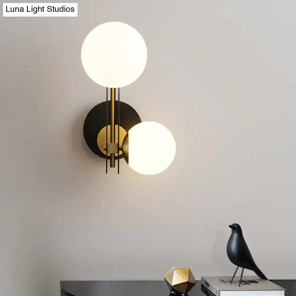 Modern black and gold milky glass wall light with direct wired electric connection and frosted glass globes in brushed brass finish