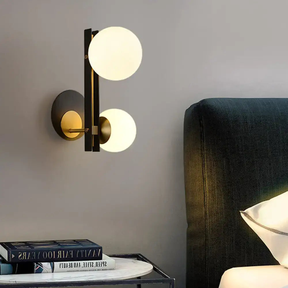 Modern black and brass wall light with two glowing milky glass shades direct wired electric for bedroom use
