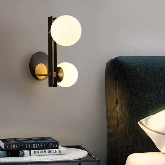 Modern black and brass wall light with two glowing milky glass shades direct wired electric for bedroom use