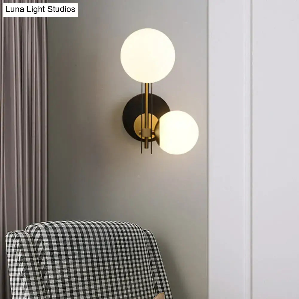 Modern black and gold wall light with milky glass globe shades and direct wired electric mounting for bedroom use